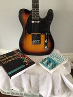 Telecaster-style sunburst electric guitar with two songwriting books on a towel-covered surface