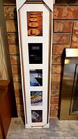 Tall white Umbra photo frame with five matted 4x6 photos in vertical arrangement leaning against brick wall near fireplace