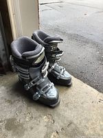 Side view of both black and gray women's ski boots with adjustable buckles and visible padding inside.