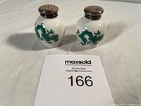 Pair of white ceramic salt and pepper shakers with silver caps and green dragon designs, positioned side by side with auction lot number card