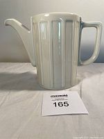 Front view of white ceramic coffee pot with vertical fluted panels, rectangular handle, and spout.
