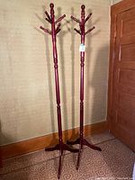 Two wooden coat racks standing next to each other against a wall, showing full height and base design.