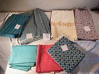 Top view of seven folded fabric pieces in different colors and patterns arranged on a white surface.