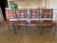 Four vintage brown leather kitchen chairs with metal frames arranged side by side on a kitchen floor.