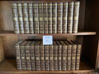 Full view of 28 brown leather-bound Harvard Classics books arranged on two shelves, showing gold embossed titles on spine.