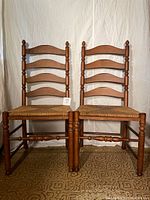 Pair of wooden ladder back chairs with woven seats, shot from the front against a white backdrop.