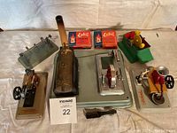 Overview of the full lot showing the Fleischmann steam engine toy, sausage maker, blacksmith toy, water wheel, two small boxes of Esbit fuel tablets, and a black handled tool.