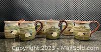 Six handpainted stoneware mugs arranged side by side; green and brown glaze with sheep motif