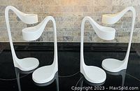 Pair of white metal candle holders side by side showing their curved, two-level design