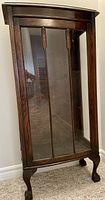 Front view of antique dark wood curio cabinet with glass front door and carved lion claw feet.