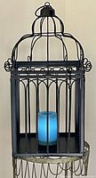 Front view of large black decorative metal bird/candle cage with battery operated blue glowing candle inside.