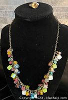 A jewellery display bust showing the colourful necklace with various coloured cube beads and the silver ring with yellow crystal on top.