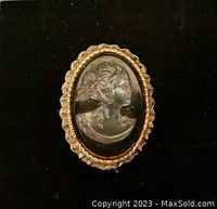Close-up of antique cameo brooch featuring a woman's profile in relief set in a gold-tone frame.