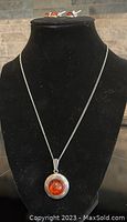 Photo of black necklace display stand with silver amber pendant. Pendant has circular silver frame with round amber center stone.