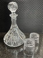 Front view of the lead-glass crystal decanter with stopper on black textured background, showing cut starburst and groove pattern.