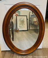 Front view of oval mirror showing bevelled glass and polished wood frame.