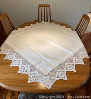 Full view of square white table cloth on wooden dining table, showing its crochet lace scalloped edges and overall shape.