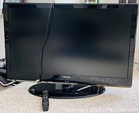 Front view of Samsung LED TV with power cord and remote on its stand.