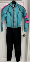Full view of ladies wetsuit jacket hanging on door, turquoise blue with pink striping, and black legs portion