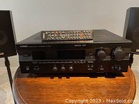 Front view of the Yamaha RX-V495 receiver with remote control on top and two speakers visible on each side.