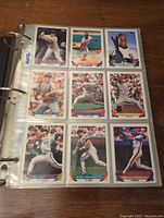 Page of baseball cards in plastic sleeves on one binder page, showing nine cards with various players in baseball uniforms, action poses, and close-up portraits.