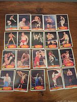 Top down view of 20 WWF wrestling cards laid out on a wooden surface showing front images of various wrestlers from 1985.
