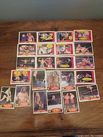 Top down view of 23 WWF wrestling trading cards laid out in rows on a wooden table showing colorful images of wrestlers in ring and portraits with captions and speech bubbles