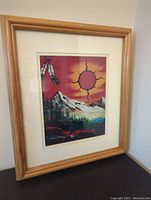 Framed Aboriginal landscape artwork showing a sun with radiating lines, mountains, pine trees, and feathers hanging in the top left corner.