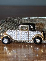 Close-up of vintage-style car brooch featuring Swarovski crystals and black enamel roof, resting on wood surface