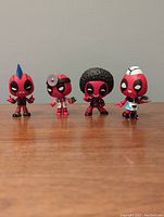 Photo showing all four Deadpool miniature bobblehead figurines side by side with distinct costumes: punk rocker, doctor, disco, and roller skate.