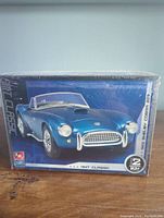 Front view of the sealed AMT Classic 1963 Shelby Cobra 289 plastic model kit box with blue car illustration.
