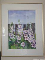 Frontal view of watercolor painting of lavender hollyhocks against a wooden fence, white double-matted and framed.