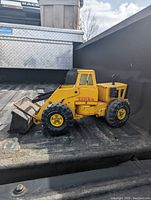 Side view of the yellow Tonka metal front loader toy showing the loader bucket and wheels.