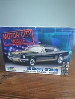 Front view of the sealed box showing black 1966 Shelby Mustang GT350H with gold stripes, Motor City Muscle branding, and Revell logo