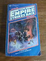 Front cover of Star Wars The Empire Strikes Back paperback novel with blue background and illustrated characters from the movie.