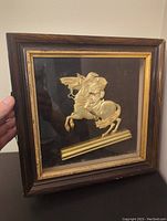 Full view of the framed piece showing the wooden frame, black background, and the golden Napoleon figure on horseback under glass.