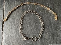 Two silver bracelets laid flat against a dark stone surface, showing entire length and design of each bracelet.