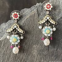 Full view of the pair of earrings against a stone background showing detailed beadwork and dangling elements.