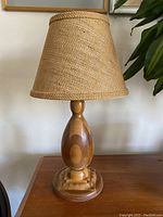 Full view of hand turned wooden lamp with burlap shade on wooden surface, unlit.