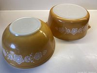 Two Pyrex mixing bowls upside down showing caramel color and white floral spring blossom pattern around sides with white bases