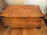 Front exterior view of closed chest showing pine planked lid, dovetailed corners and central bail handle.
