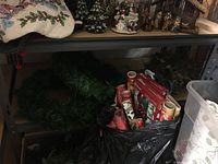 Lower shelf with wreaths, holiday wrapping paper rolls, and miscellaneous holiday decor in bags