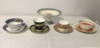 Front view of the four varied teacups and saucers arranged in a line, showing different patterns and colors.