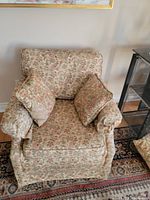 Front view of small arm chair showing floral Ashley style fabric and throw pillows.