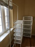 Photo showing multiple white plastic closet storage organizers: a tall shelving unit with 6 slotted shelves and a stackable basket unit with 4 tiers.