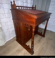 Side view of desk showing leather-topped tilt lid, spindle gallery, turned legs and left-side cabinet