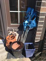 Four items visible: three garden pots of different styles and colors, plus a folded blue chair leaning against a brick wall.
