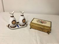 Two white Limoges decorative jars with gold and brown detailing on matching tray, alongside floral petite point metal jewelry box