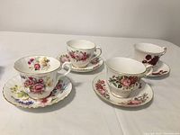 Four floral patterned fine bone china tea cups each paired with matching saucers, displayed at an angle showing floral designs and gold trim.
