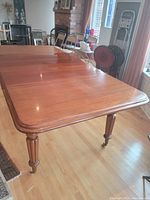 Photo showing the top surface and one rounded corner of the mahogany dining table with turned leg and caster wheel.